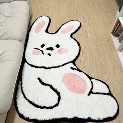 Tapis blanc rigolo en forme de lapin devant un canapé blanc.